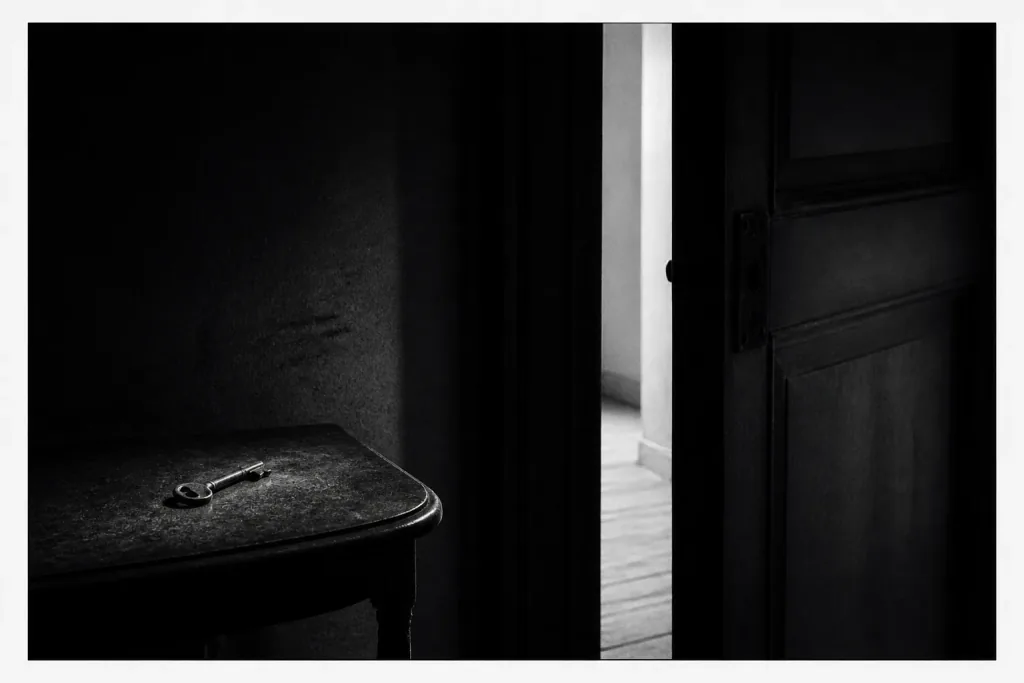 A key on a table beside a wooden door sitting slightly ajar